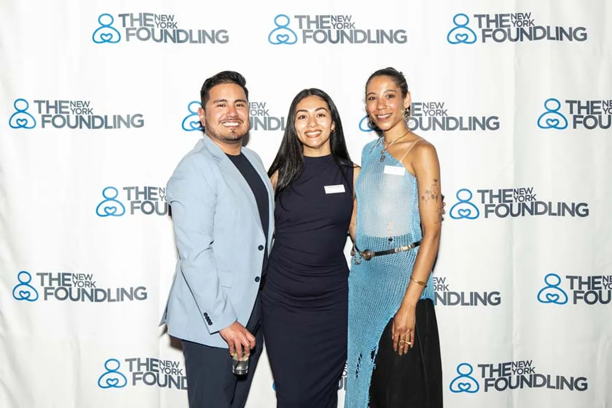 The New York Foundling members posing for a photo in front of a back drop of the NYF logo.